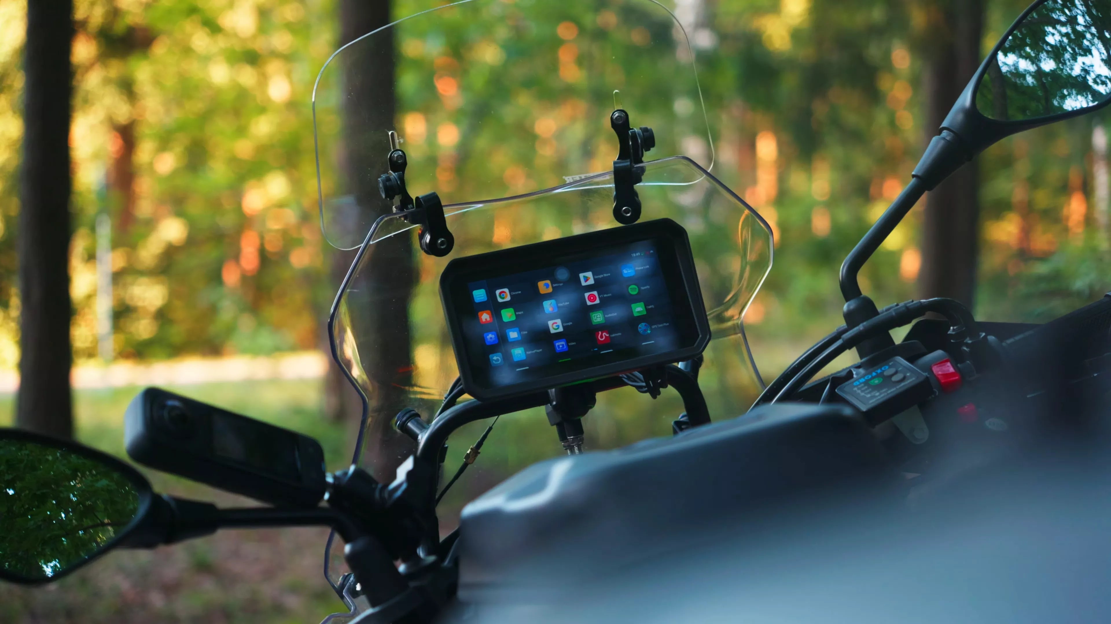 Motorcycle with a smartphone mount displaying colorful app icons, surrounded by trees.